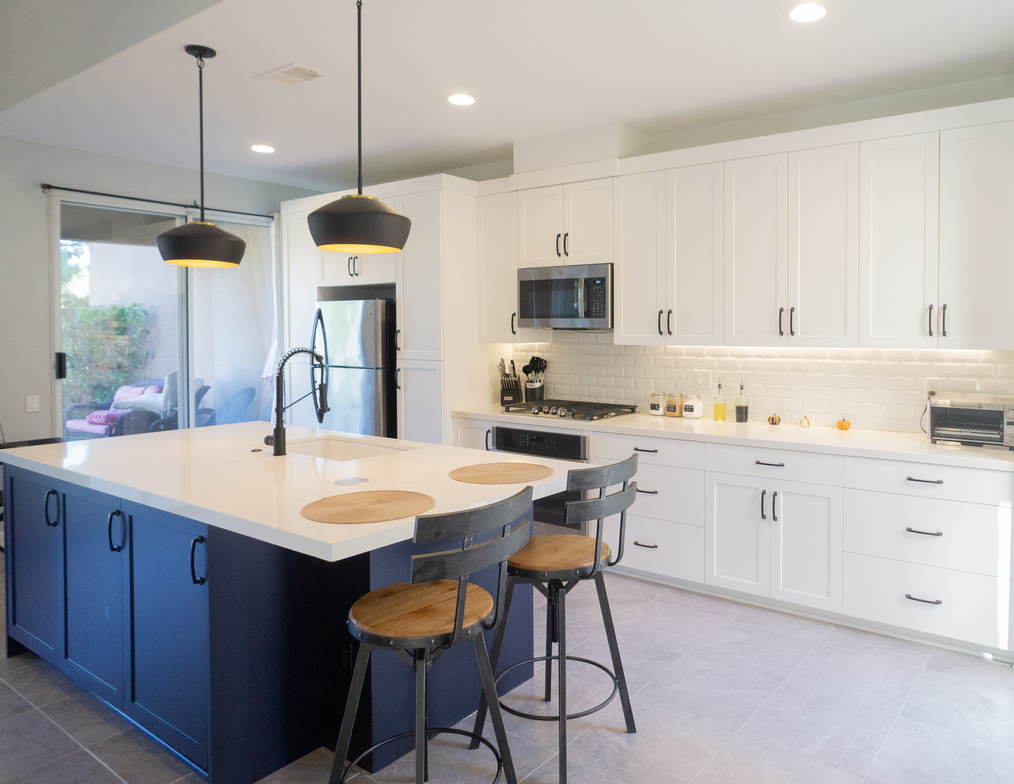 Palm Desert Whole-Home Renovation — navy island kitchen with black pendant lights, white upper cabinets, subway tile