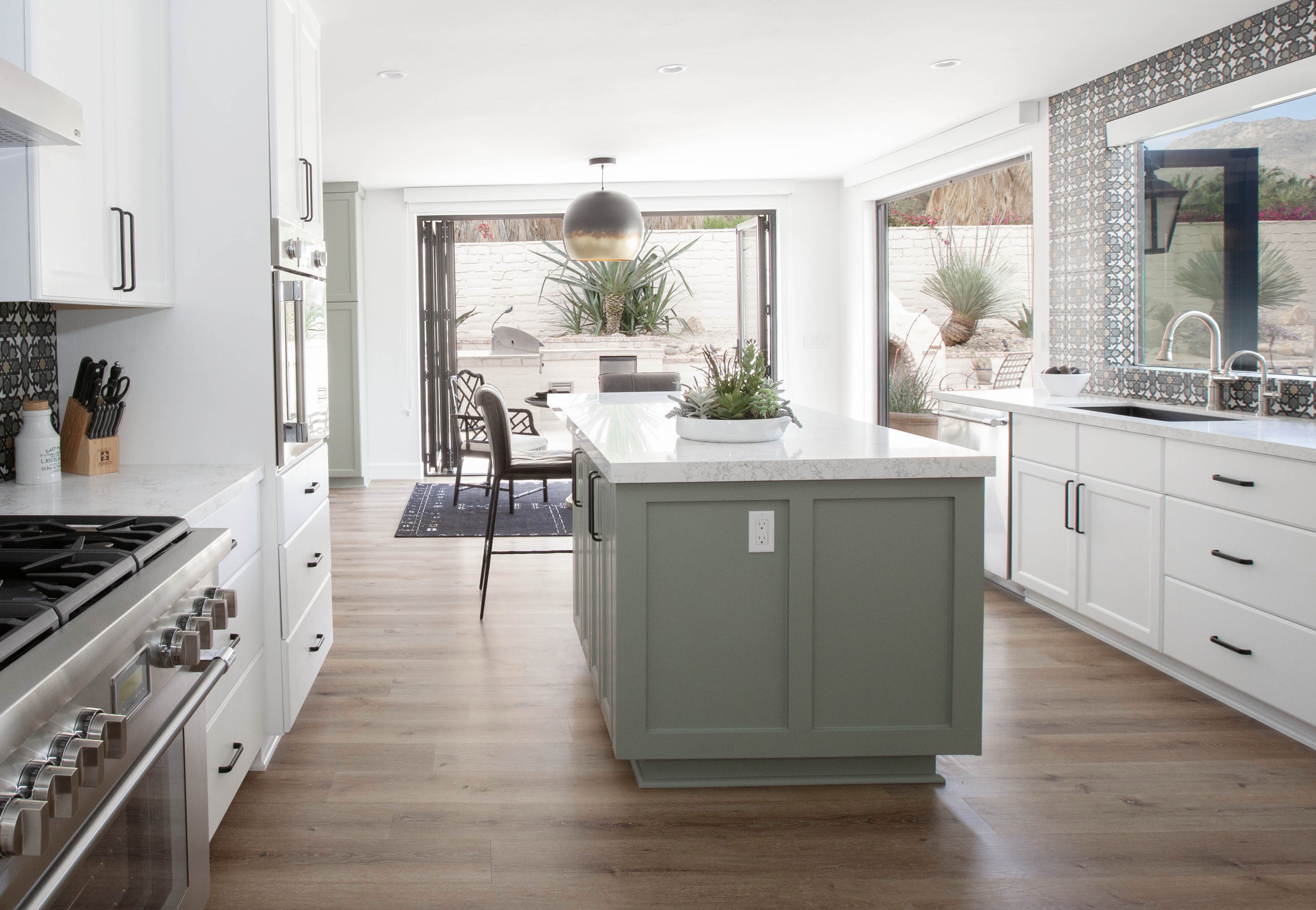 Room Addition & Whole-Home Renovation — wide kitchen with sage green island, bifold doors open to desert pool patio