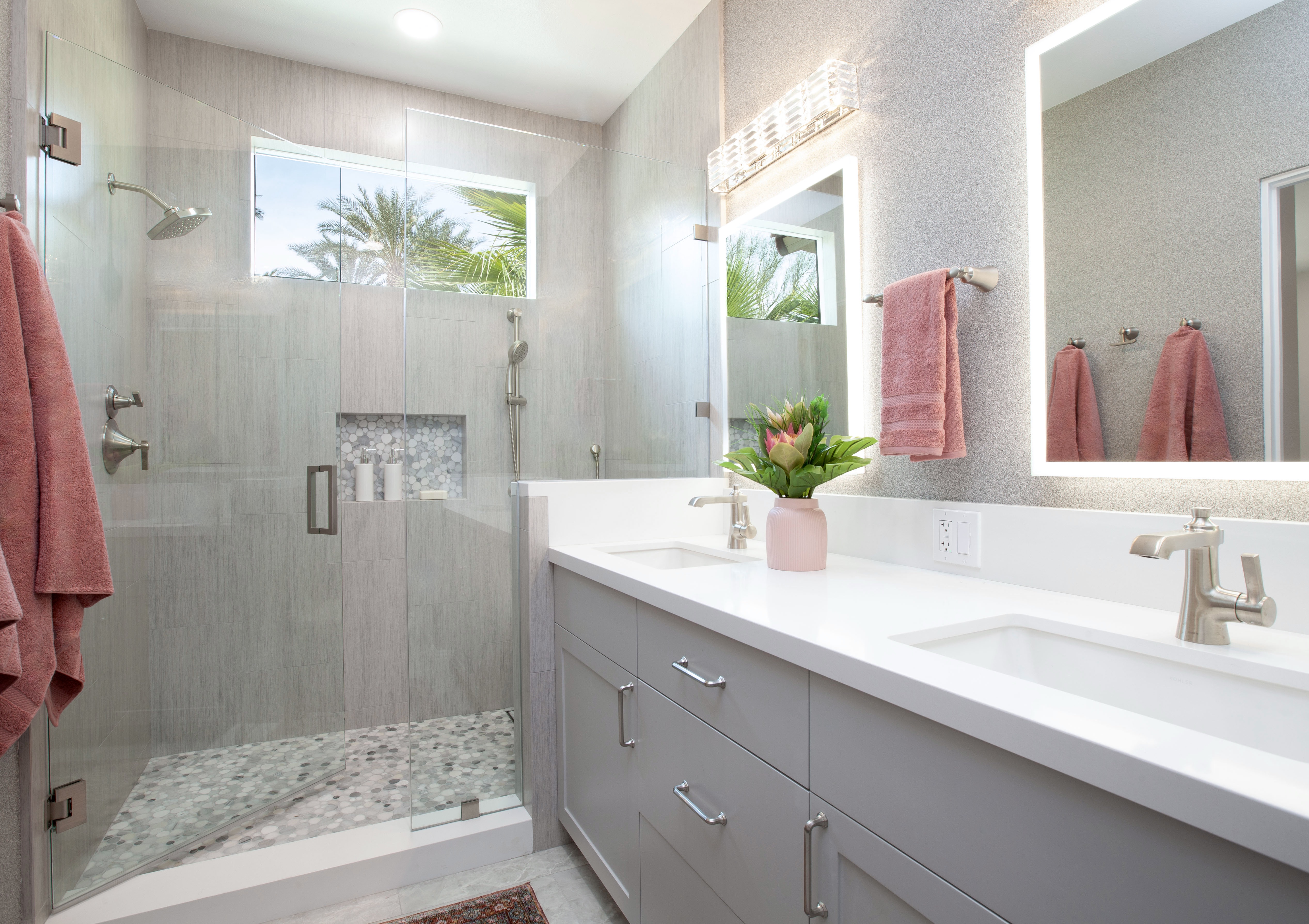 Multi-Bathroom Renovation — pink and gray bath with dual sink, glass shower and lit mirrors